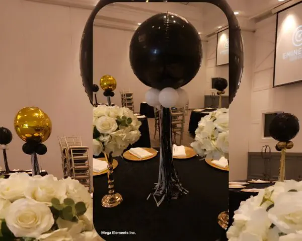 Table centerpiece with black and gold balloon columns and white floral arrangements