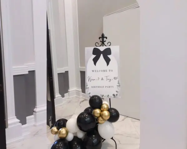 Welcome sign with black bow and white floral balloon base for birthday party