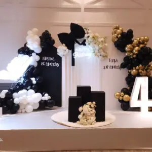 Black and white balloon backdrop with "Kāpras 1st birthday" custom sign