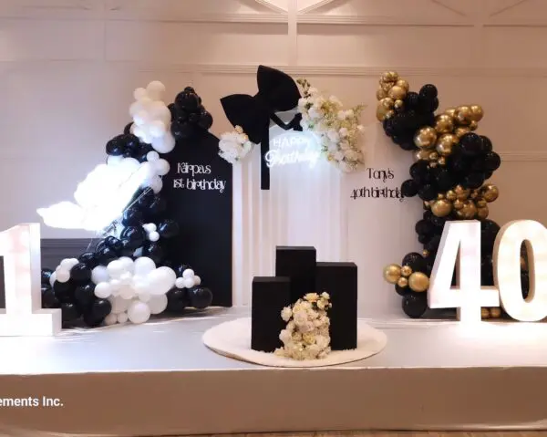Black and white balloon backdrop with "Kāpras 1st birthday" custom sign