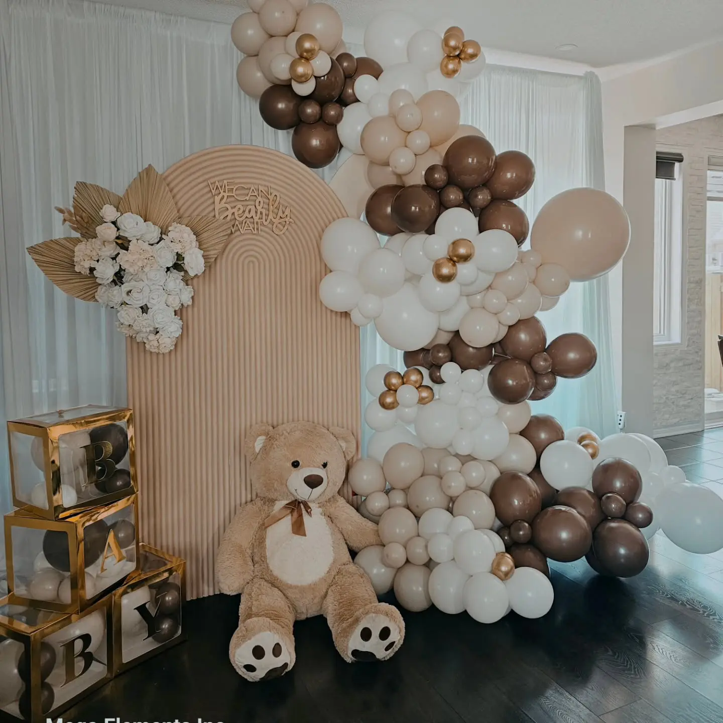 Neutral indoor bridal shower balloon garland with white, brown, and gold balloons, teddy bear, and wooden panel backdrop in Brampton