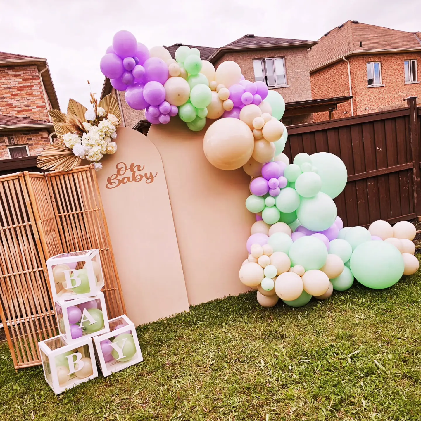 Pastel bridal shower balloon garland setup outdoors with “Oh Baby” sign and wooden panels in Brampton