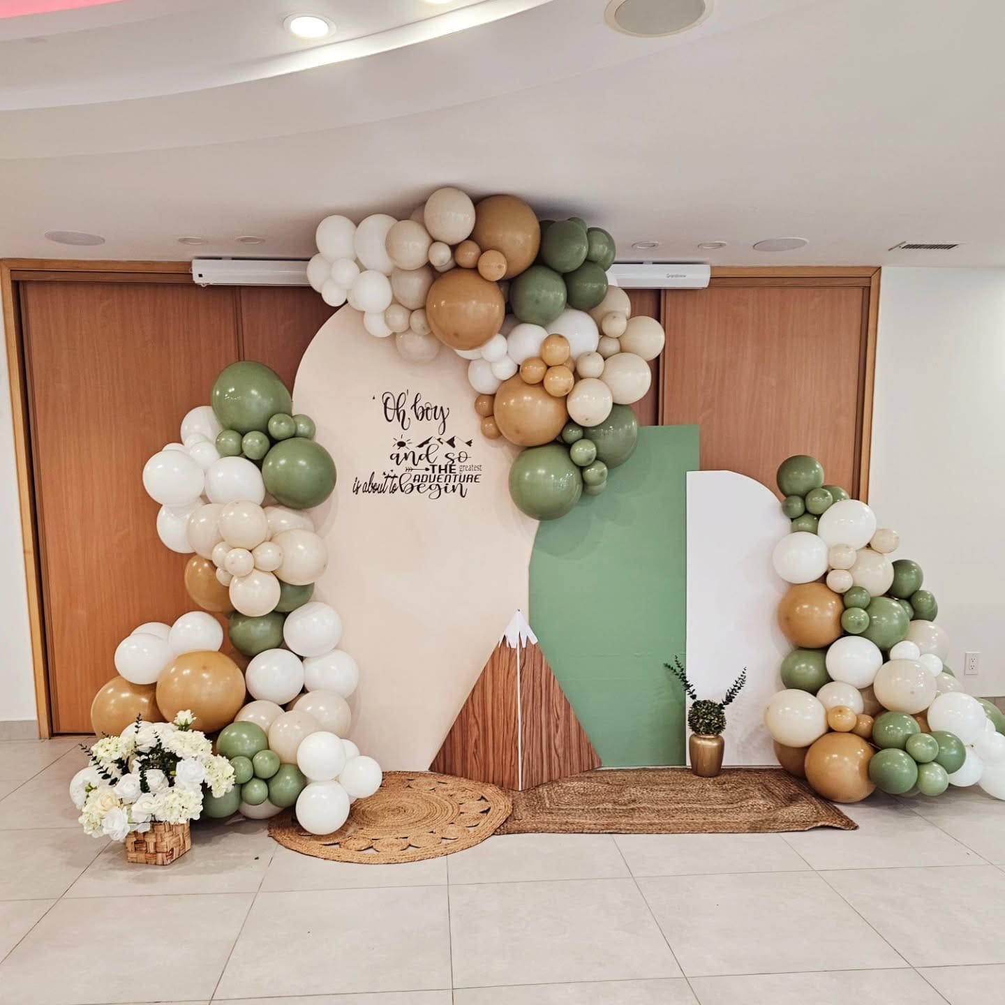 Adventure-themed bridal shower decor with green, gold, and beige balloon garlands, floral basket, and custom mountain backdrop in Brampton
